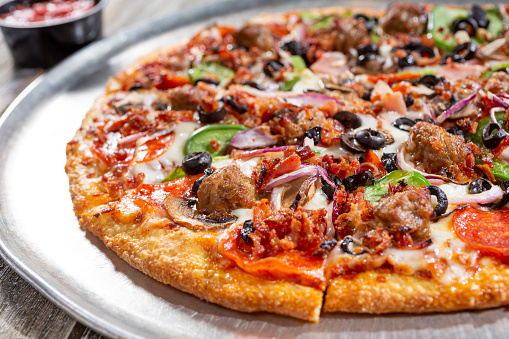 A view of a meat and veggie pizza pie, in a restaurant or kitchen setting.