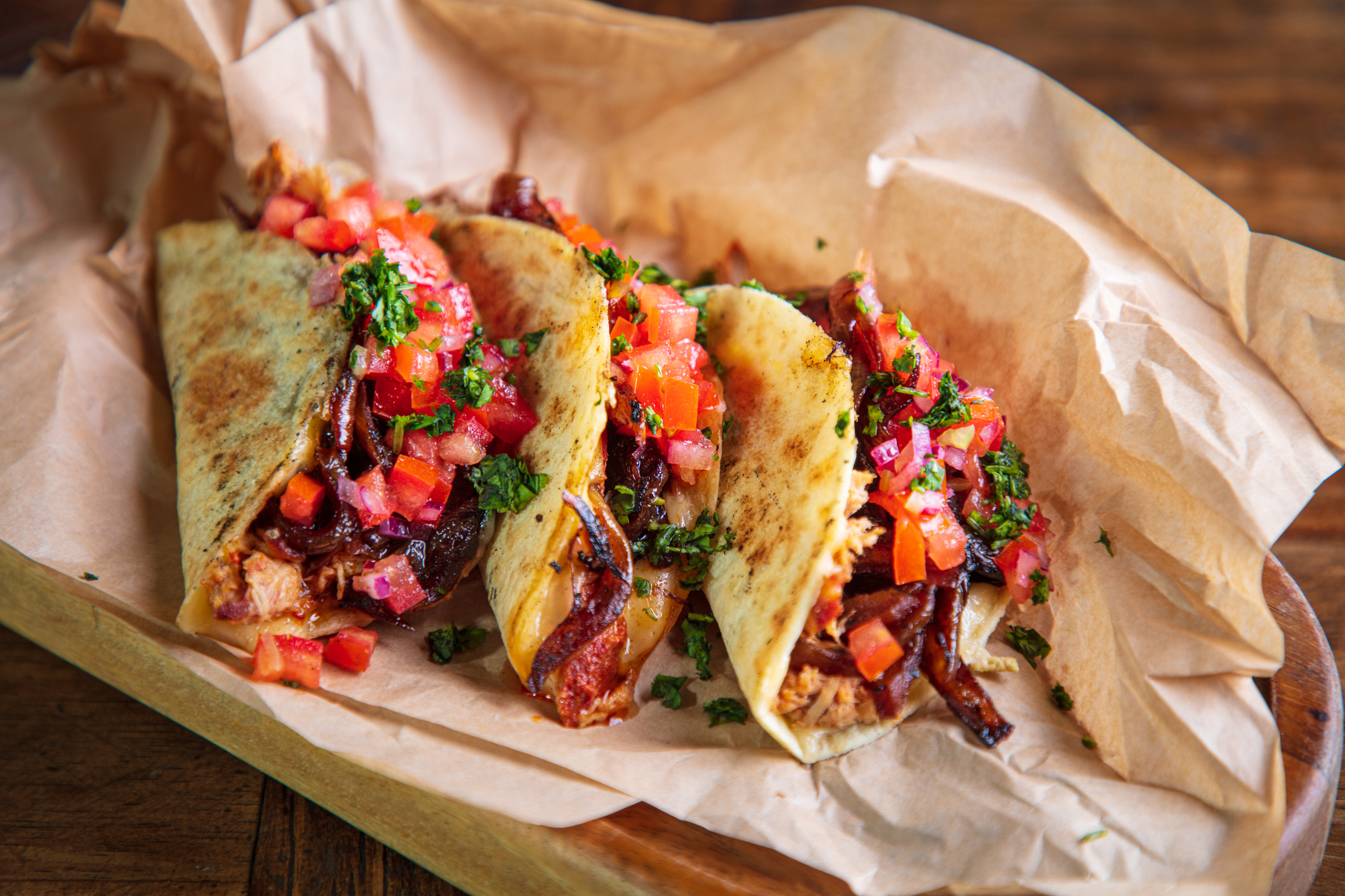 Serving of tacos with shredded roast pork and cheese filling on brown paper in wooden plate
