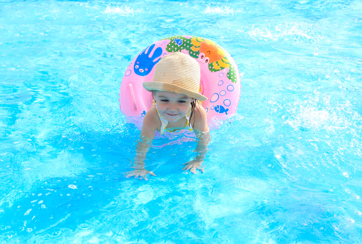 Happy little girl playing with colorful inflatable ring in the outdoor pool on a hot summer day